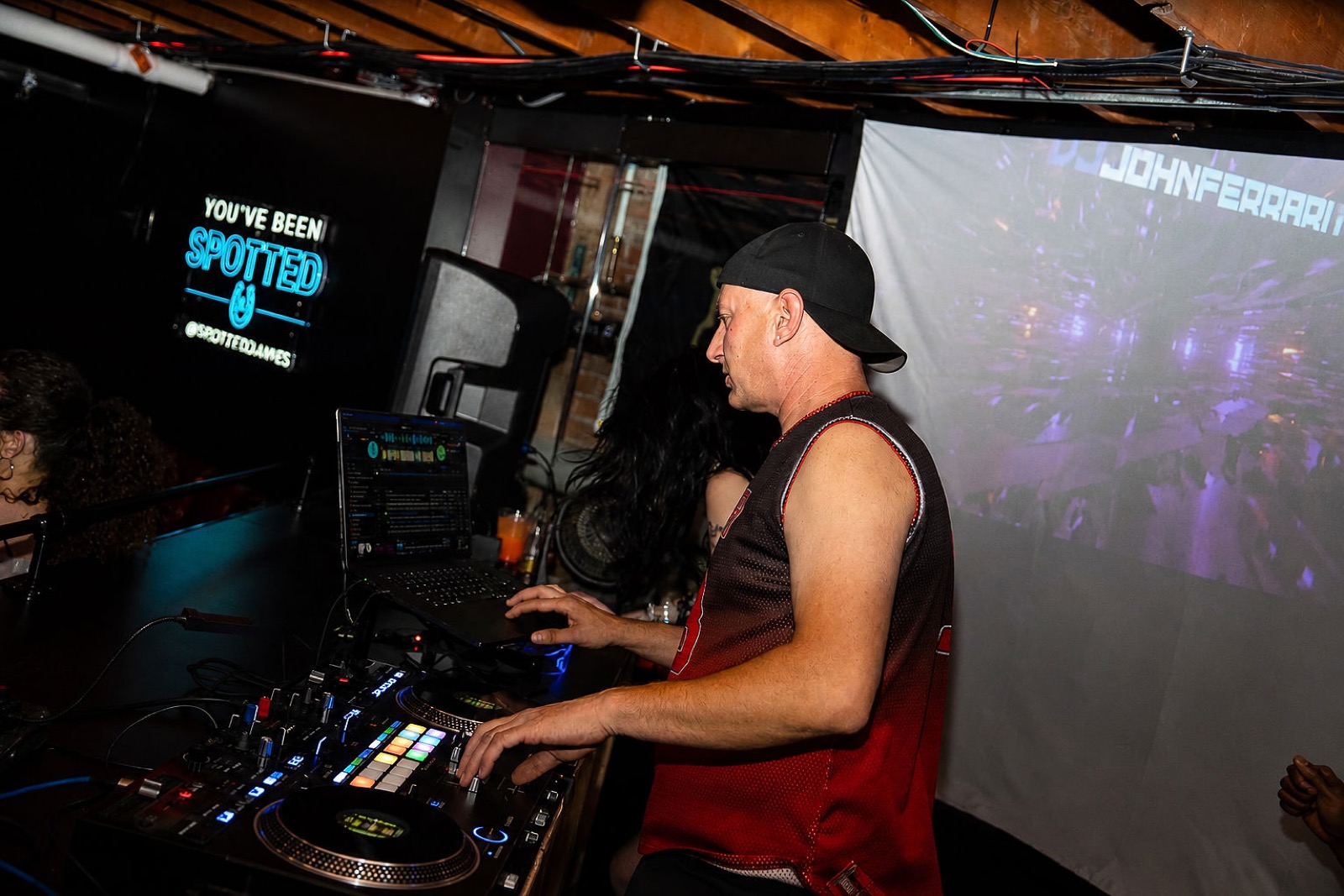 DJ mixing beside the You've Been Spotted neon sign