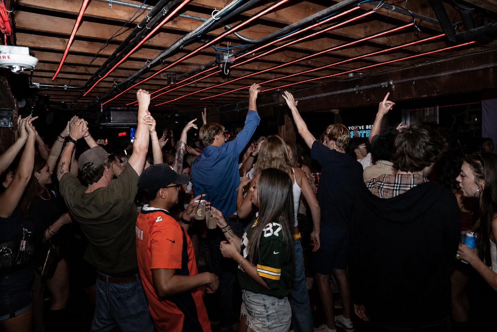 Crowd with hands in the air under the red neon ceiling lights
