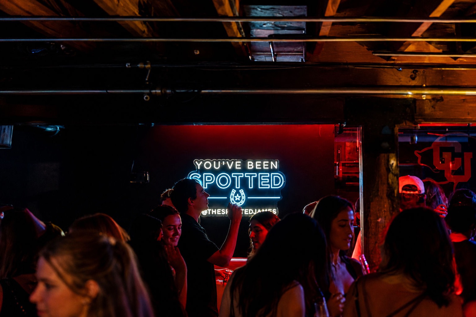 The You've Been Spotted neon sign glowing above the crowd beside the CU logo
